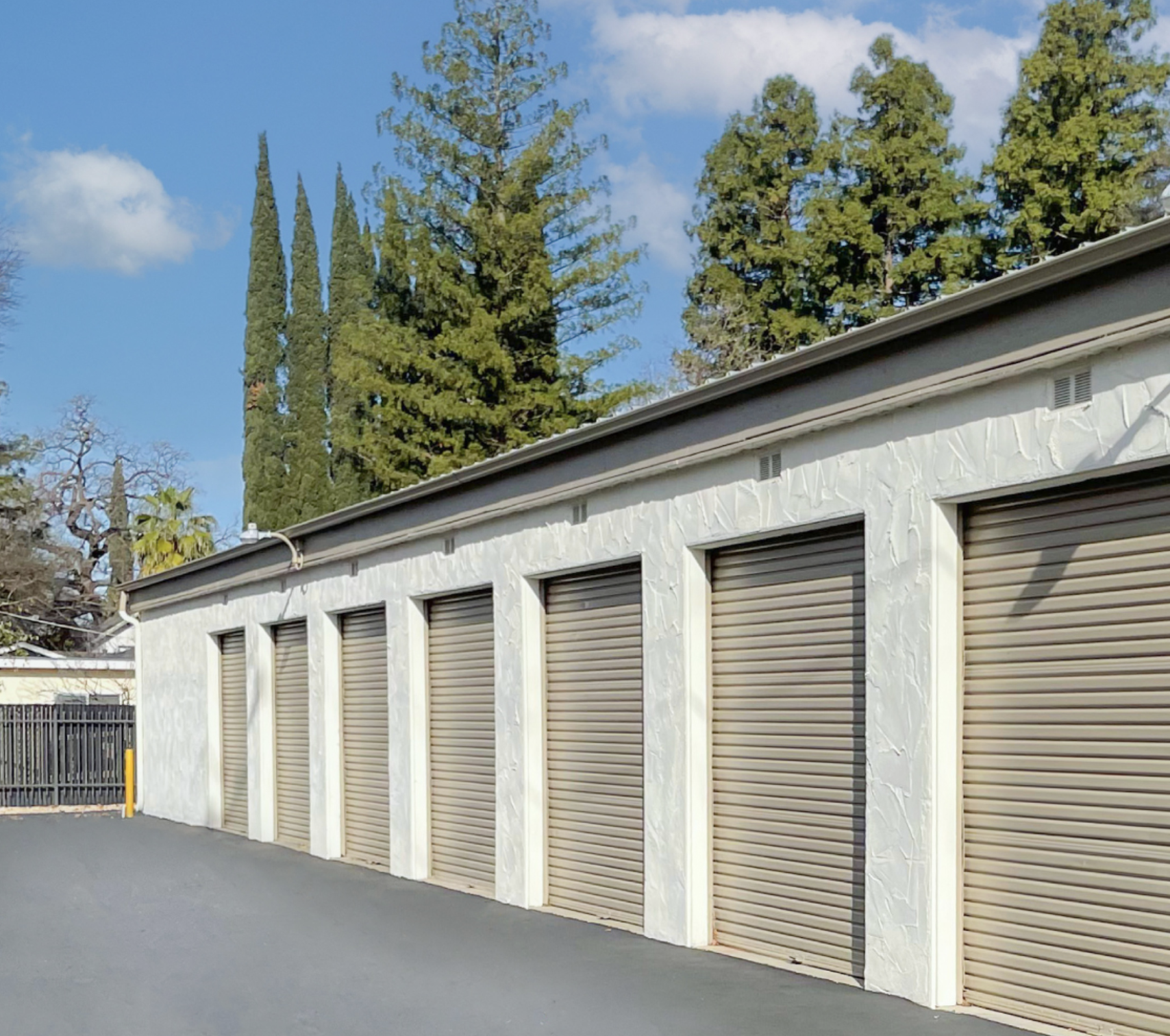 Mini Storage image - dark beige doors with light beige walls and green trees in the background
